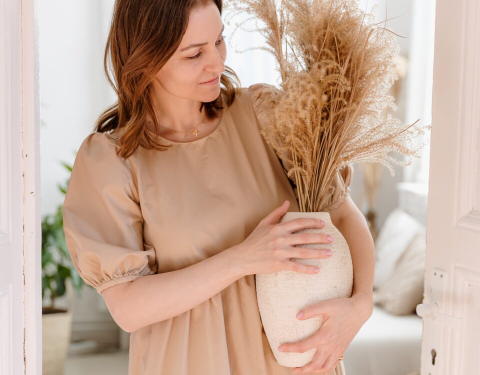 Femeie ținând o vază cu plante uscate într-un interior luminos – Casă în spirit slow living